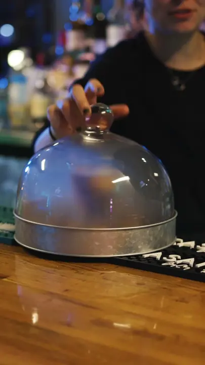 A chef lifting a cloche at a restaurant bar